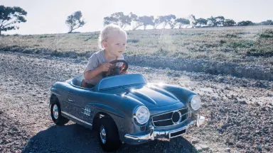 Blonder Junge sitzt in fahrendem kleinen Kinder-Auto